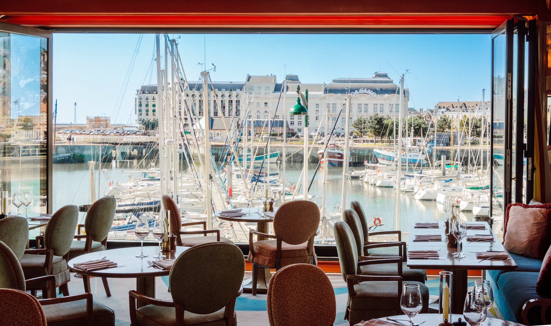 Intérieur du restaurant deauville vue sur mer et sa vue sur le port de plaisance, avec décoration années 50. Le restaurant Le Deauville et sa décoration d'inspiration années 50, pensée par Martin Brudniski.